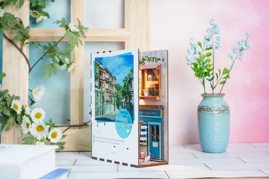Houten boekensteun met straatafbeelding en miniatuur café, met bloemen op de achtergrond.