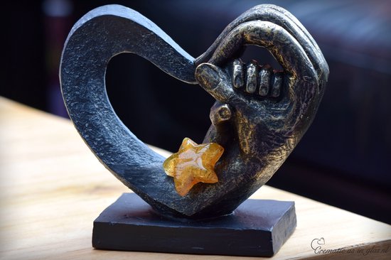 Zwarte hartvormige urn met gouden handen, met een amberkleurige glazen ster.