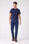 Blauwe Wrangler jeans, regular fit, gedragen met donkerblauw T-shirt met klein rood logo en rode schoenen.