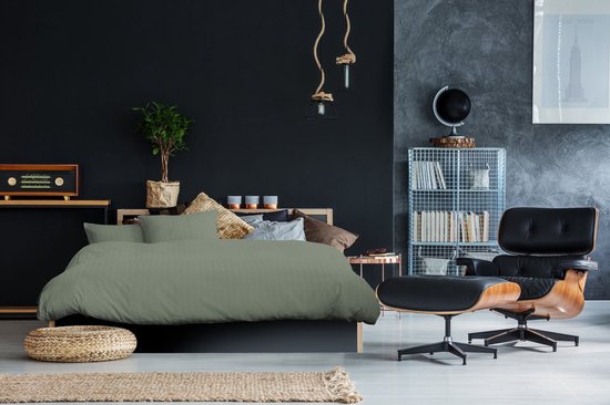 Groen satijnen dekbedovertrek met verticale strepen op een bed in een donkere slaapkamer.