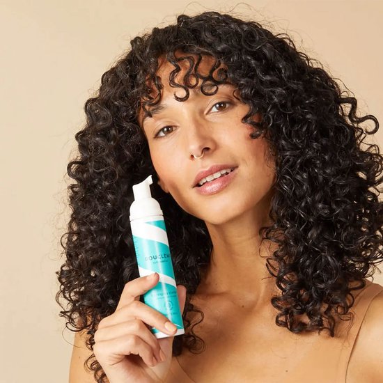 Vrouw met krullend haar houdt een witte fles met blauwe strepen vast.