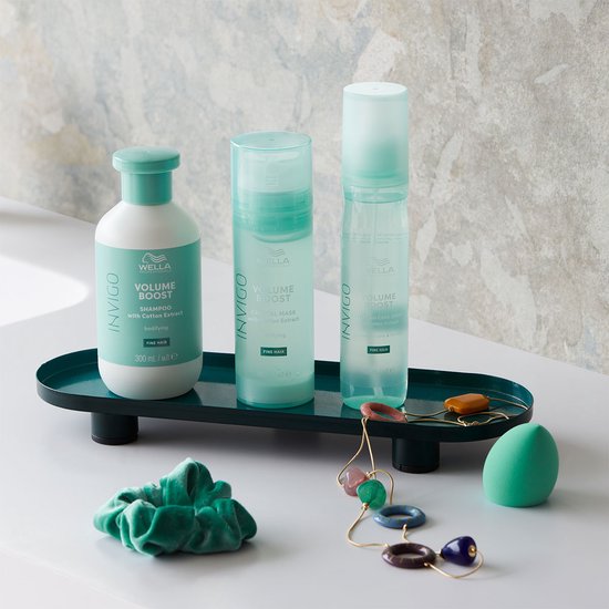 Wella Invigo Volume Boost shampoo en conditioners, met een groen schuimende scrunchie, kralensnoer en een groene spons.