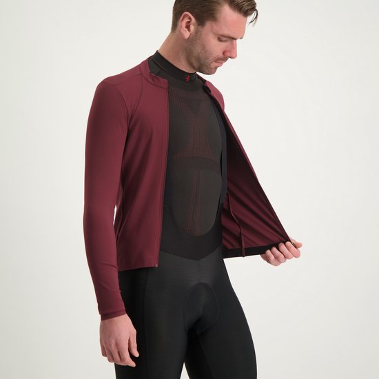 Man die een donkerrood wielershirt met lange mouwen aantrekt over een zwart shirt met mesh-structuur.