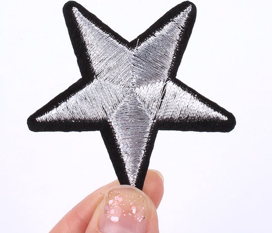 Een hand met glitter nagellak houdt een zilverkleurige ster-patch met zwarte rand vast.