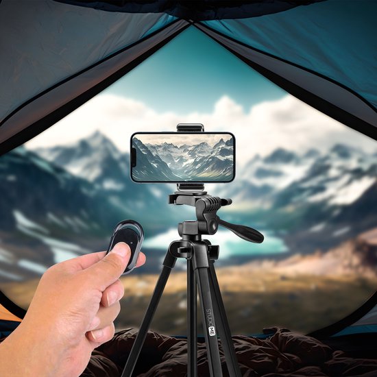 Zwarte statief met smartphone en afstandsbediening, vanuit een tent met bergen op de achtergrond.