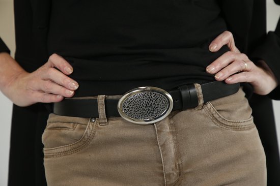 Zwarte riem met ovalen zilverkleurige gesp met zilverkleurig gaasdetail, gedragen door een model in beige broek.