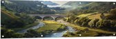Tuinposter – Rivier - Bergen - brug - Water - Stenen - Gras - Bomen - Wolken - 150x50 cm Foto op Tuinposter (wanddecoratie voor buiten en binnen)
