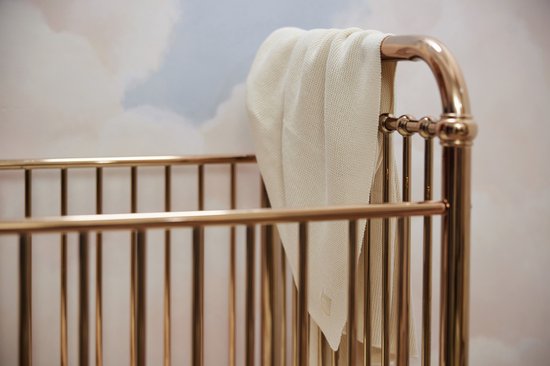 Couverture en maille crème drapée sur les barreaux d'un lit de bébé doré.