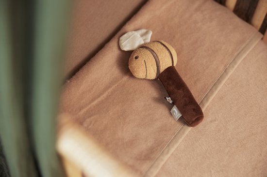 Een biscuitkleurige wiegdeken waarop een zachte rammelaar in de vorm van een bij ligt.