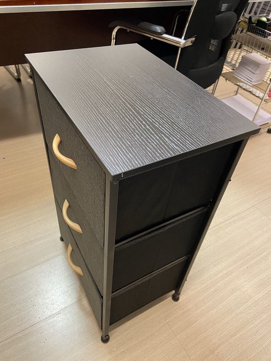 Donkergrijs stoffen nachtkastje met 3 lades en houten handgrepen, een lade is open.