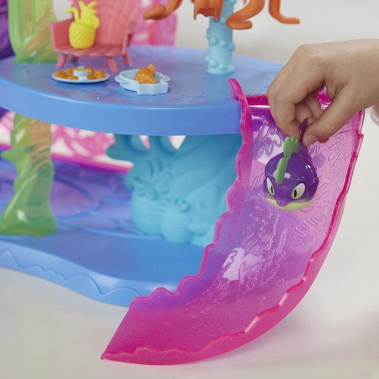 Een hand houdt een paarse speelgoedvis met grote ogen vast bij een roze glijbaan.