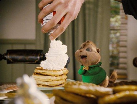 Een Chipmunk in een groen vest kijkt naar een stapel pannenkoeken met slagroom.