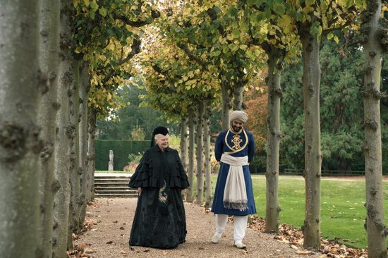Koningin Victoria (Judi Dench) en Abdul (Ali Fazal) lopend over een bospad.