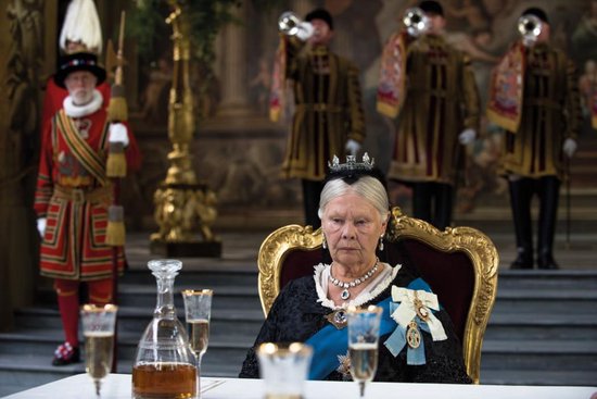 Koningin Victoria (Judi Dench) zittend aan een tafel met mannen in ceremoniële kledij op de achtergrond.