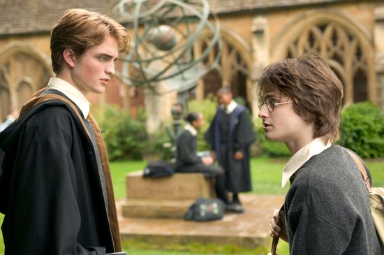Twee jongens, Harry Potter en Cedric Diggory, staan buiten en praten, studenten op de achtergrond.
