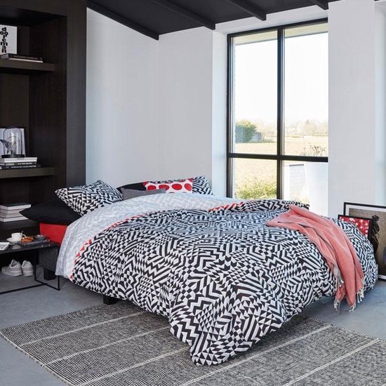 Chambre moderne avec un lit fait d'une housse de couette géométrique noire et blanche et d'un plaid rose.