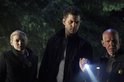 Drie personen met serieuze gezichten in de nacht, een man in het midden schijnt met een zaklamp.