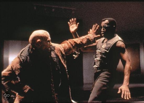 Wesley Snipes in zwart vest tegenover een kaal hoofd personage met bruine jas.