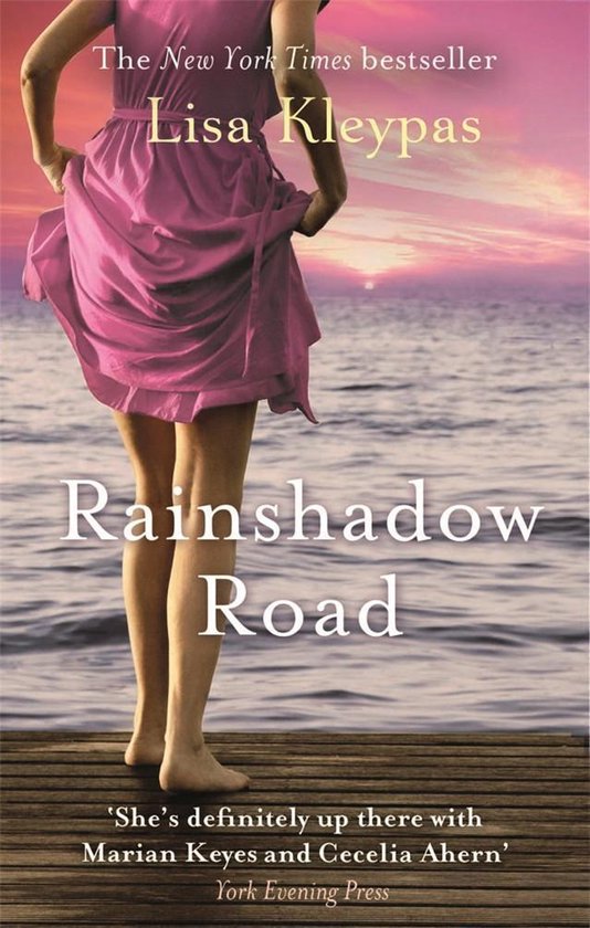 De New York Times bestseller Lisa Kleypas Rainshadow Road, een vrouw in een roze jurk op een pier bij zonsondergang.