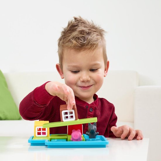 Een jongen met een rode trui speelt met het spel. Hij plaatst het bruine huis op een groene balk.