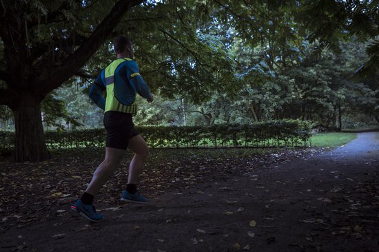 Man joggend in het donker met een fluoriserend geel hesje over een blauw shirt.