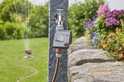 GARDENA besproeiingscomputer op stenen pilaar met kraan. Tuin met bloeiende planten.