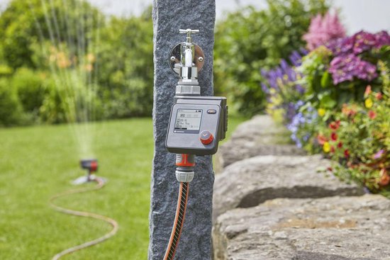 GARDENA besproeiingscomputer op stenen pilaar met kraan. Tuin met bloeiende planten.