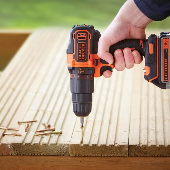 Hand houdt een zwarte en oranje accuboormachine vast, schroeft in houten planken.