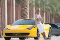 Een man in een gestreept shirt en witte shorts leunt tegen een gele Ferrari.
