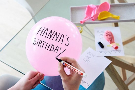 Een persoon gebruikt een zwarte edding 400 marker om "HANNA'S BIRTHDAY" op een roze ballon te schrijven.