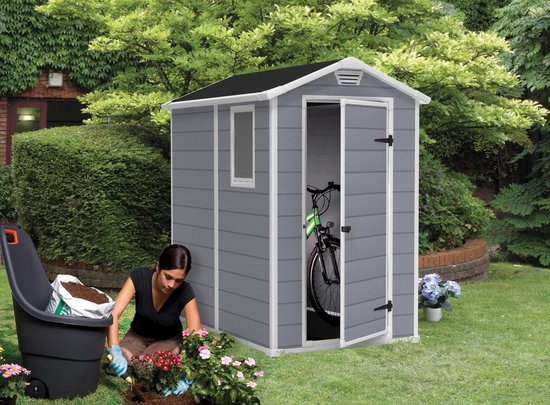 Grijs Manor Pent 6x4 tuinhuis met schuin dak, open deuren met fiets erin. Vrouw tuiniert voor de deur.