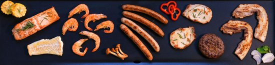Bovenaanzicht van een zwarte bakplaat met zalm, garnalen, worstjes, vlees en groenten.