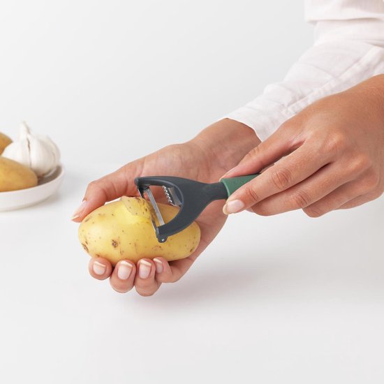 Handen schillen een aardappel met een groene dunschiller met donkergrijs lemmet. Zesteur zichtbaar.