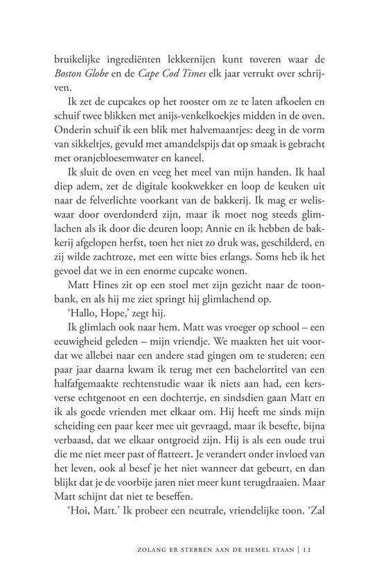 Een vrouw, gekleed in een witte coltrui en een rode jas, staat met haar rug naar een tafel, en houdt een kopje koffie vast.