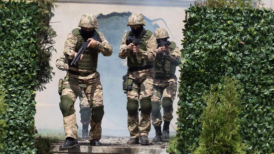 Drie soldaten in camouflagekleding en kogelwerende vesten lopen door een muur.
