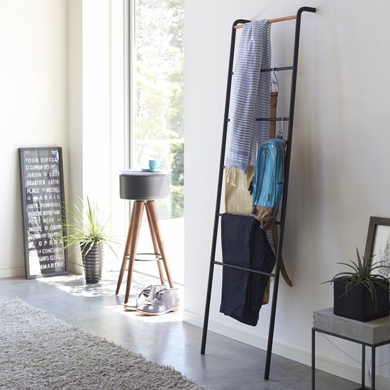 Zwarte ladderrek met kledingstukken: een gestreept textiel, riem, blauwe rugzak, broek en spijkerbroek.
