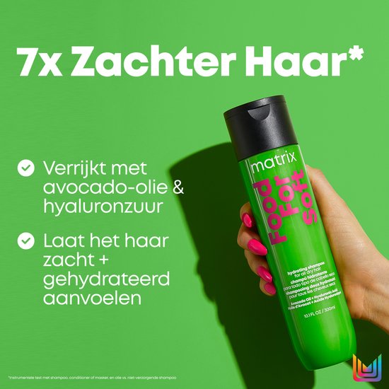 Une main aux ongles rose vif tient une bouteille vert vif de shampooing Matrix Food For Soft, avec du texte sur l'huile d'avocat et l'acide hyaluronique.