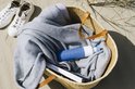 Blauwe Dopper drinkfles in een rieten mand op het strand, met een deken en boeken.