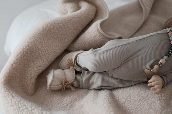 Baby in een crèmekleurige wollen deken, liggend op zijn buik, met grijze kleding en schoentjes.