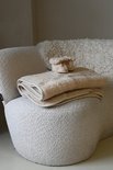 Crèmekleurige wollen deken op een stoel met bijpassende babyschoentjes erop.