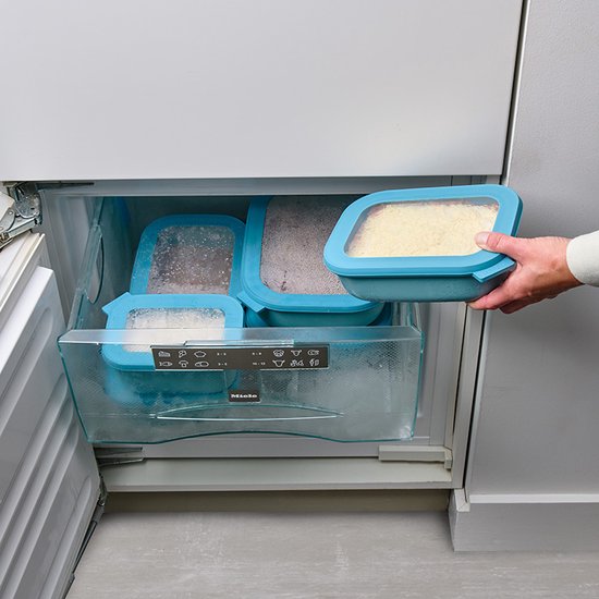 Une main prend une boîte de conservation bleu clair avec du riz dans un congélateur. D'autres boîtes bleu clair sont à l'intérieur du congélateur.