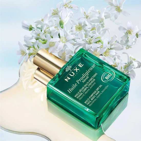 Groene Nuxe Huile Prodigieuse Néroli fles met gouden dop, met witte bloesems en olie.
