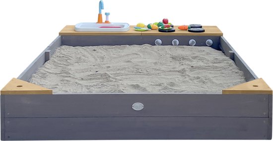Grijze zandbak met een houten speelkeuken met aanrecht, kraan, knoppen en speelgoedgroenten.
