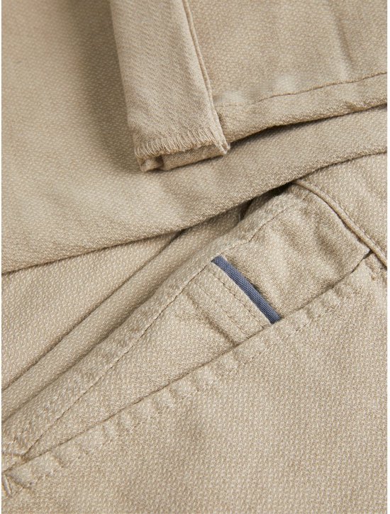 Detail van de crèmekleurige chino broek, textuur en steekzak.