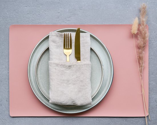 Gedekte tafel met zalmroze placemat, grijs bord met bestek en een gedroogde plant.