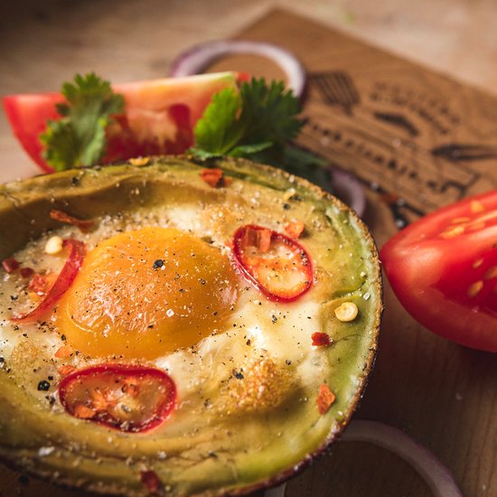 Een cederhouten plank met een gevulde avocado, tomaat, rode ui en brood.