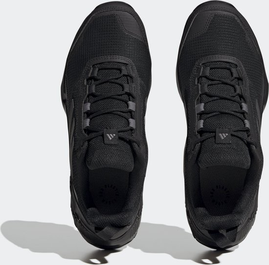 De bovenkanten van twee zwarte dames wandelschoenen met veters en zwarte Adidas-strepen.