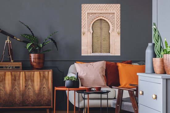 Une porte marocaine couleur sable avec des détails dorés et une sculpture sur pierre complexe, accrochée au-dessus d'un canapé avec des coussins orange et rouge.