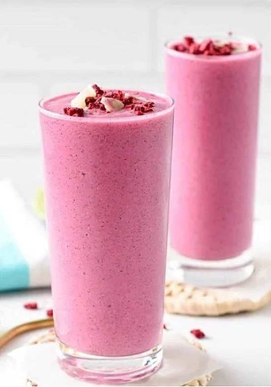 Twee glazen roze smoothie, gegarneerd met rood fruit en kokosschaafsel.