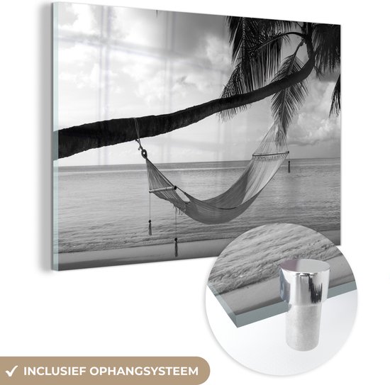 MuchoWow® Glasschilderij 60x40 cm - Schilderij acrylglas - Hangmat vastgeknoopt aan een palmboom bij een strand - zwart wit - Foto op glas - Schilderijen